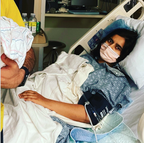 Kriti Lodha in a hospital bed during her postpartum psychosis hospitalization, holding her newborn daughter's hand